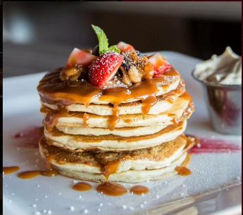 A stack of pancakes with strawberries and caramel